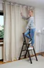 A woman is standing on a step stool to adjust curtains. Anteprima dell’immagine prodotto