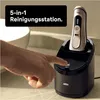 A hand is pressing a button on a black charging and cleaning station for an electric shaver. Náhled obrázku produktu
