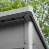 Close-up of the corner of a gray metal garden shed, with green foliage in the background. Anteprima dell’immagine prodotto
