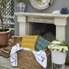 An outdoor patio scene with a fireplace, cushions in a basket, and flowers in a planter. Produktbild-Vorschau