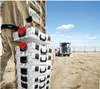 A construction worker carrying a stack of toolboxes at a construction site with a van in the background. Náhled obrázku produktu