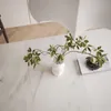 A close-up overhead view of a marble-patterned table with a white vase holding a green plant and a book with a small plant on top. Produktbild-Vorschau