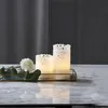 Two LED candles with a lace-like pattern are placed on a golden tray with a white flower and green leaves. Podgląd zdjęcia produktu