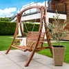 A wooden garden swing set is placed on a patio in a backyard with a house and manicured lawn in the background. Náhled obrázku produktu