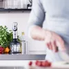 A person is preparing food in a kitchen, with a blender and vegetables on the counter. Voir les images du produit