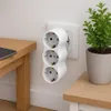 A white triple socket adapter plugged into a wall socket, next to a wooden table and a potted plant. Produktbild-Vorschau