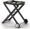 A black foldable grill stand with wheels, shown from a diagonal angle against a white background. Náhľad obrázku produktu