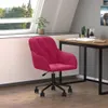 A pink velvet office chair is placed next to a wooden desk in a room with a large window. Náhled obrázku produktu