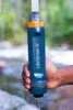 A hand holding a water filter over a stream. Produktbild-Vorschau