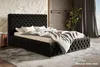 A luxurious bedroom with a tufted black bed, dressed in white and gray bedding, set against a textured stone wall and dark wood paneling. A plant and curtains add to the ambiance. Náhled obrázku produktu