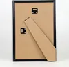 The back of a black picture frame with a brown cardboard backing and a stand attached. Produktbild-Vorschau
