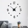 A wall clock with black numbers and hands on a white wall, with a grey sofa and a potted plant in the foreground. Náhled obrázku produktu