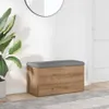 A storage bench with a gray upholstered top and a wood-grain finish is placed against a white wall, next to a large potted plant and a doorway. Produktbild-Vorschau