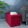 A red storage ottoman sits on a tiled floor next to a gray sofa, with a plant in the background. Náhled obrázku produktu