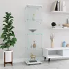 A tall, narrow glass display cabinet with four shelves, showcasing decorative items. It is placed in a room with a plant and a low cabinet. The background is a plain wall. Produktbild-Vorschau