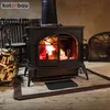 A wood-burning stove with a fire burning inside, placed on a wooden floor with a basket of firewood next to it. Náhľad obrázku produktu