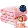 A folded pink blanket with unicorn and princess motifs, a glowing unicorn graphic, and a young girl holding a smaller blanket. Podgląd zdjęcia produktu