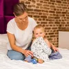 A woman and a baby are sitting on a bed. The baby is holding a blanket in its mouth. Produktbild-Vorschau