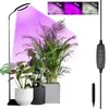 A ring-shaped LED grow light illuminates several potted houseplants. The light is adjustable in height and has multiple modes. Produktbild-Vorschau