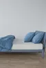 A bed with blue bedding and pillows against a white wall. Produktbild-Vorschau