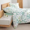 A neatly made bed with floral patterned bedding and pillows, next to a bedside table with vases. Produktbild-Vorschau