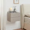 A floating nightstand with two drawers is mounted on a white wall next to a bed. The nightstand has a concrete-like texture and is decorated with a candle, a book, a vase with flowers, and a cup of coffee. Anteprima dell’immagine prodotto