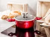 A red pot with a glass lid sits on a black stovetop, with bread in the background. Podgląd zdjęcia produktu