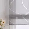 A close-up view of a grey roman blind with a white curved stripe pattern, with a bouquet of white flowers in the lower left corner. Produktbild-Vorschau