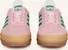 A front view of a pair of pink Adidas Gazelle Bold W sneakers with green stripes and a tan sole. Produktbild-Vorschau