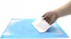 A hand is placing a white pad onto a blue absorbent mat. Produktbild-Vorschau