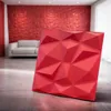 A red 3D wall panel is displayed in a modern living room setting with a sofa and a red textured wall in the background. Produktbild-Vorschau