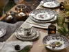 A table setting with plates, cups, cutlery, and candles, decorated with pine cones and greenery. Náhľad obrázku produktu