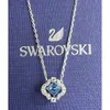 A Swarovski necklace with a blue crystal pendant is displayed on a blue textured background with the Swarovski logo and name. Produktbild-Vorschau