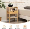 A wooden nightstand with a drawer and shelves is placed next to a bed. Decorative items like a vase with flowers, a small speaker, and books are on the nightstand. The image also features icons representing different home decor styles at the bottom. Náhled obrázku produktu