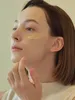 A close-up shot of a person applying a yellow cream to their cheek. Voir les images du produit