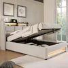 A bed with its storage compartment open, showing the mattress lift mechanism and the storage space underneath. The bed is in a bedroom setting with artwork on the wall and a window in the background. Náhled obrázku produktu