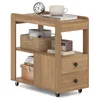 A wooden side table with two drawers and open shelves, displaying various items like books, toilet paper, a clock, and a mug. Produktbild-Vorschau