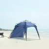 A blue beach tent set up on a sandy beach with the ocean in the background.