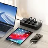 A laptop, tablet, and smartphone are connected to a black power strip with multiple outlets and USB ports, suggesting a charging station setup. Produktbild-Vorschau