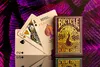 A deck of Bicycle Peacock playing cards is displayed with three cards fanned out in front of the deck, set against a vibrant purple and black background. Produktbild-Vorschau