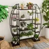 A circular metal plant stand filled with various potted plants, placed on a wooden floor indoors. Podgląd zdjęcia produktu