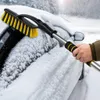 A person is using a snow brush with an ice scraper to clear snow from a car window during winter. Produktbild-Vorschau