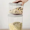 A hand is placing a clear food storage container filled with cereal on top of another identical container filled with pasta. Produktbild-Vorschau