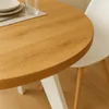 A close-up view of a round wooden dining table with a white leg, next to a white chair. A placemat, plate, and glass are visible on the table. Produktbild-Vorschau