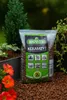 A bag of BIOVITA KERAMZYT (expanded clay) is shown outdoors, surrounded by plants and flowers, with some of the product spilled on the ground. Produktbild-Vorschau