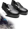 A pair of black safety overshoes is shown in the foreground, with a person using a jackhammer in the background, suggesting a construction or industrial setting. Produktbild-Vorschau