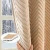 A hand is holding a beige quilted curtain, revealing a snowy forest scene through a window behind it. A close-up inset shows the texture of the curtain. Produktbild-Vorschau