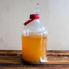 A large plastic container filled with a yellow liquid, sitting on a wooden surface. Produktbild-Vorschau