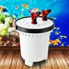 A white aquarium filter with red connectors sits on a wooden surface in front of a blurred aquarium scene. Podgląd zdjęcia produktu