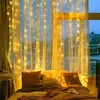 A cozy bedroom scene with string lights draped over sheer curtains, illuminating a bed with pillows and a blanket. Produktbild-Vorschau